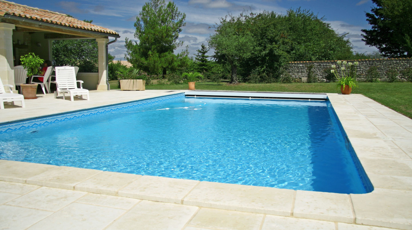 Piscine coque polyester bleu turquoise suspendue par une grue lors de son installation dans un jardin, avec deux ouvriers en gilets de sécurité.